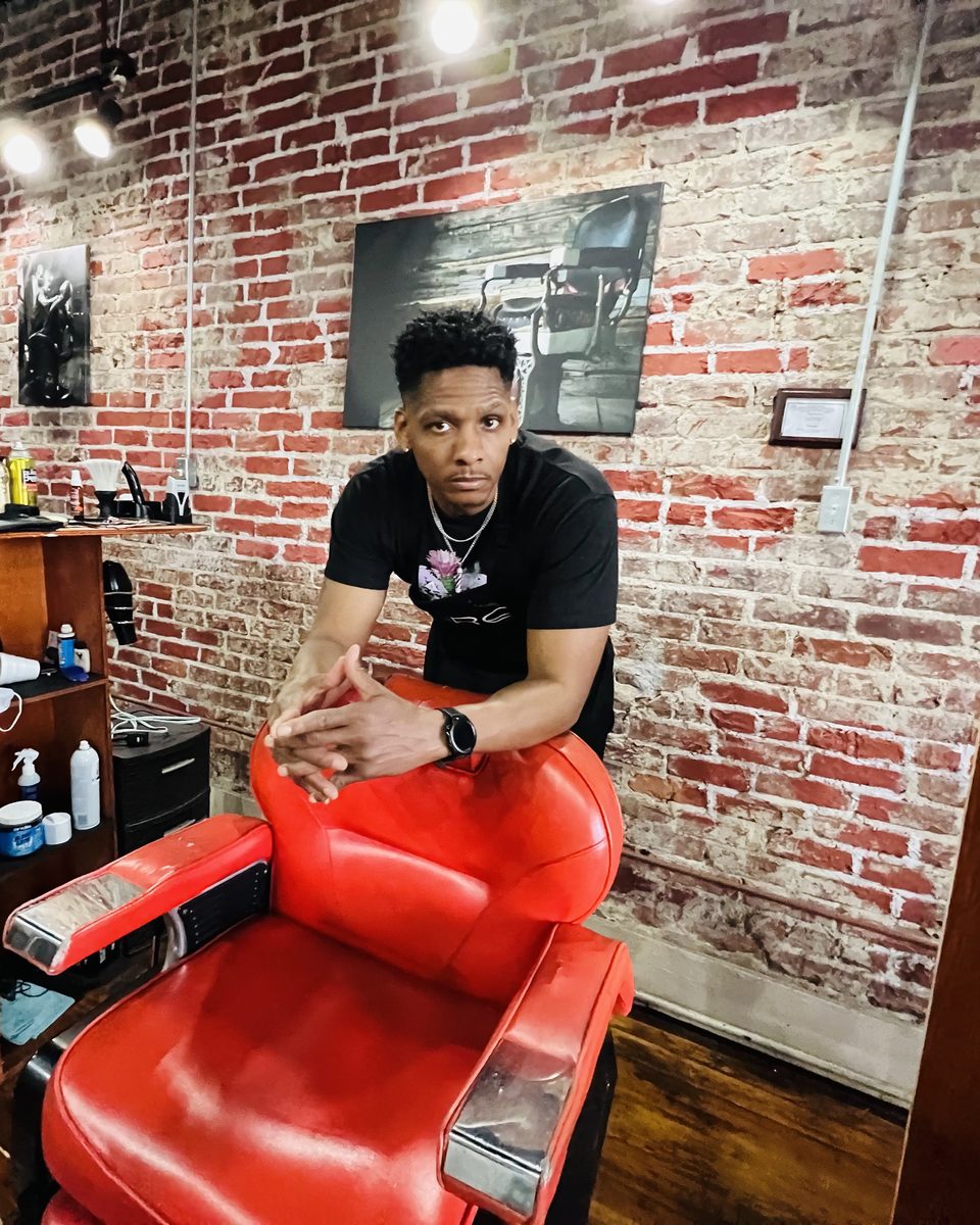 Corey Cooper leaning on his red barber chair inside Pure Upscale